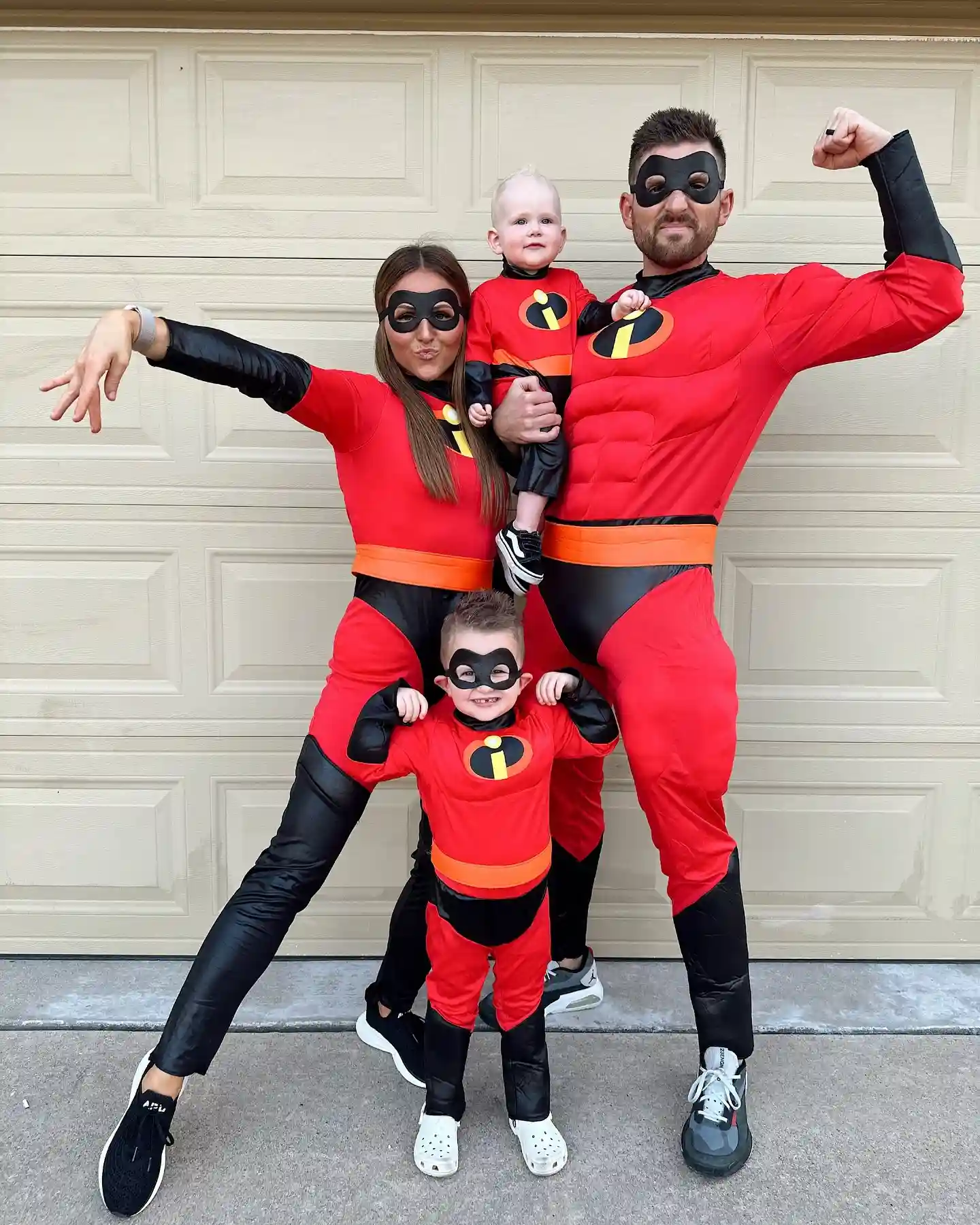 Family of four in matching red Incredibles costumes with masks, the baby held up and the toddler in front