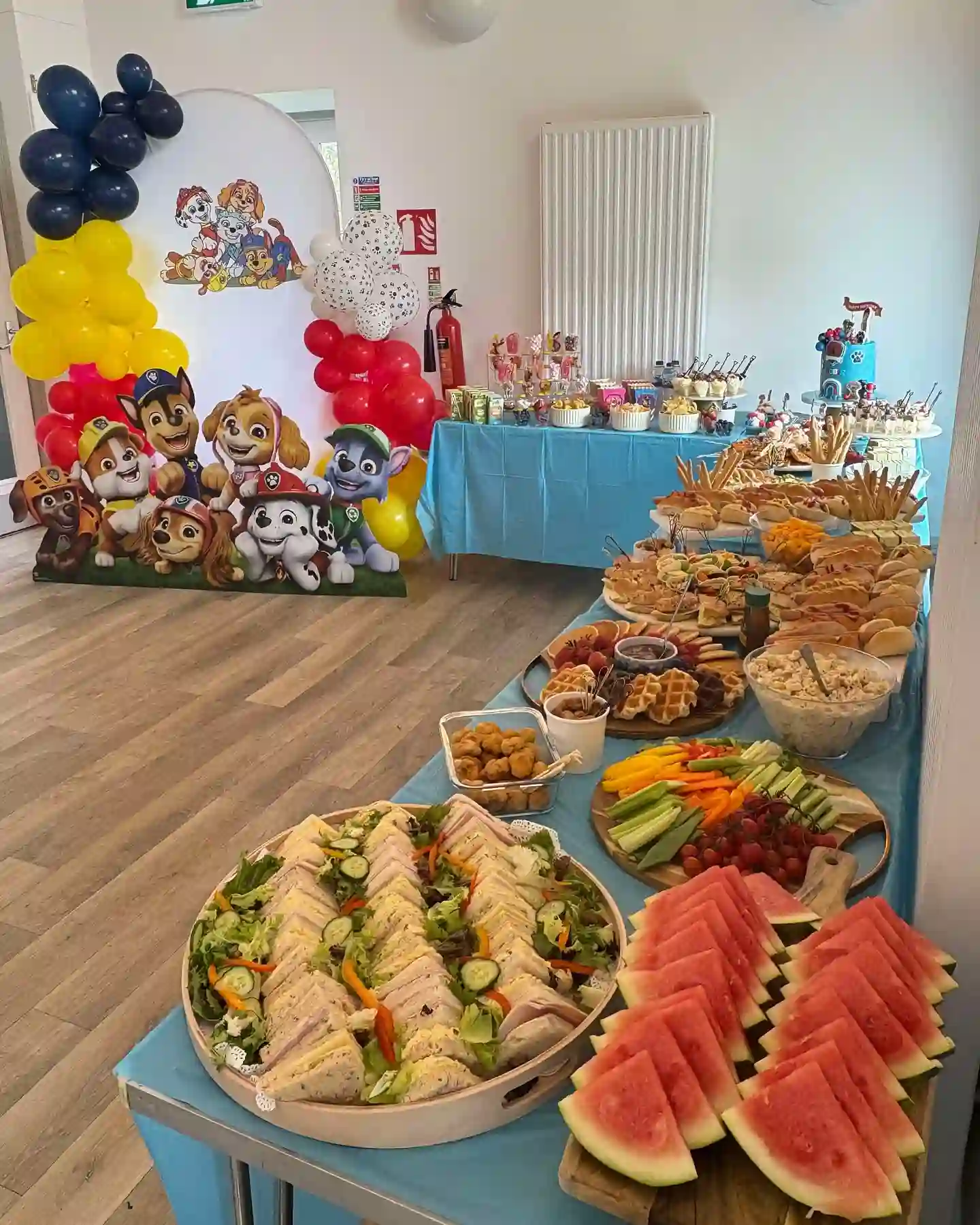 Birthday party food ideas: Paw Patrol birthday buffet with sandwich triangles, watermelon wedges and a veggie board on a blue tablecloth