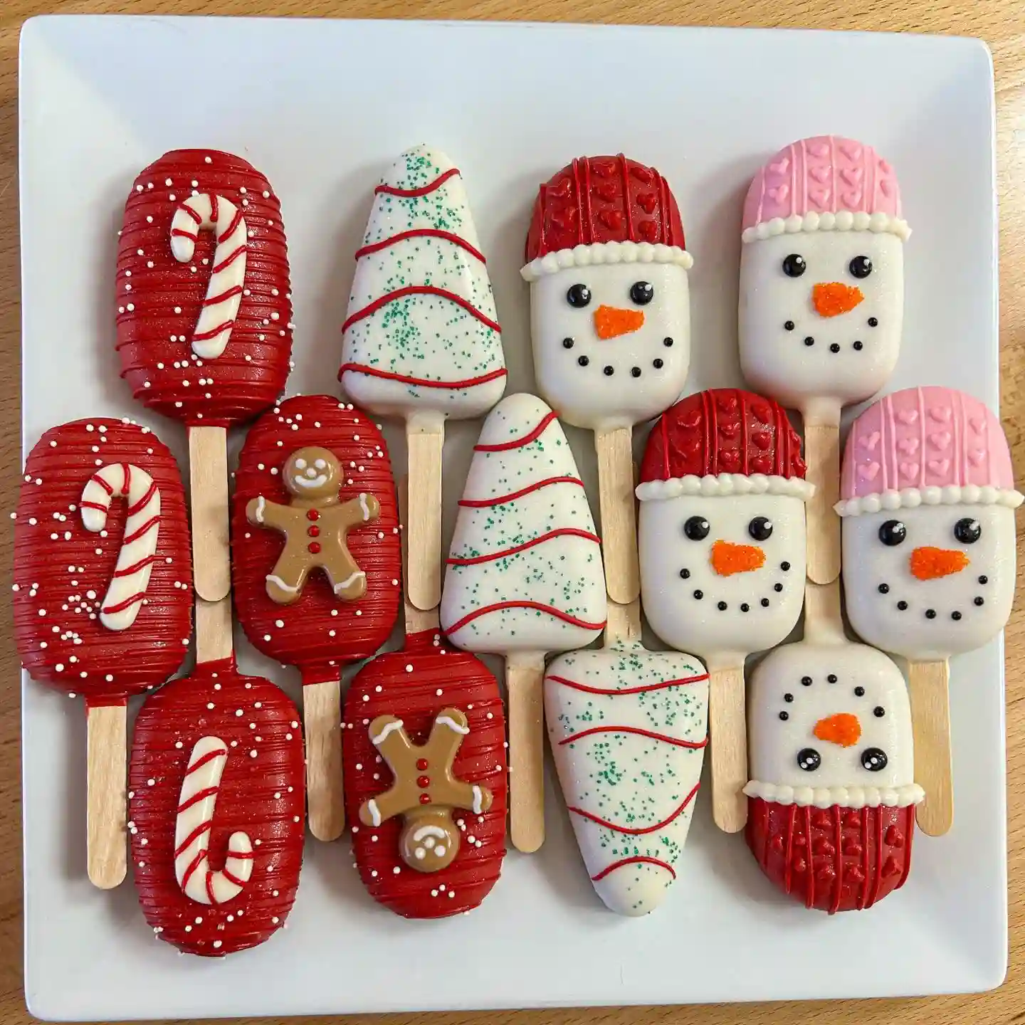 White box of mixed Christmas cookies including gingerbread sandwiches, iced gingerbread faces, a snowman, jam hearts and red and green swirls with greenery and ornaments