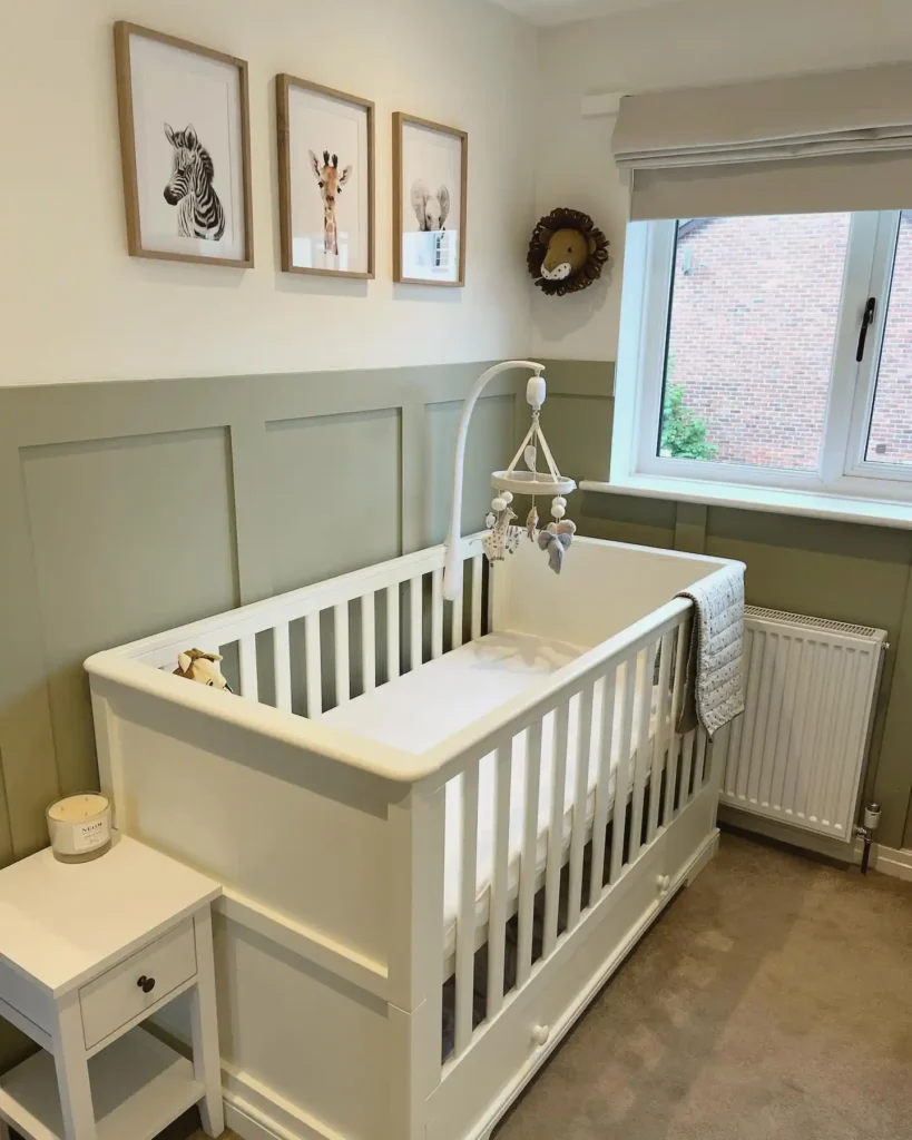 Nursery with sage green wall paneling, a white crib and three framed baby animal prints