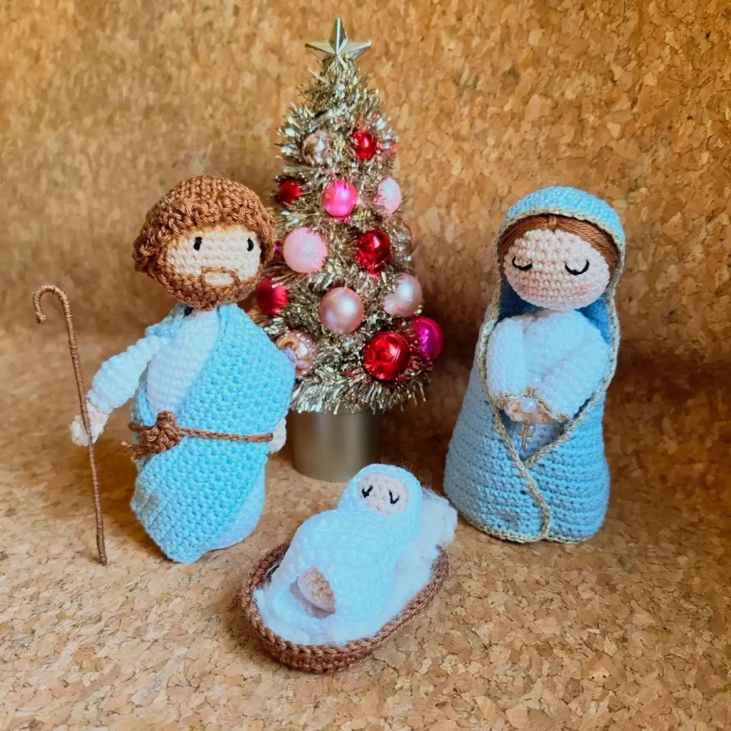 Soft crochet nativity set with Mary, Joseph and baby in a woven basket beside a small gold tinsel tree