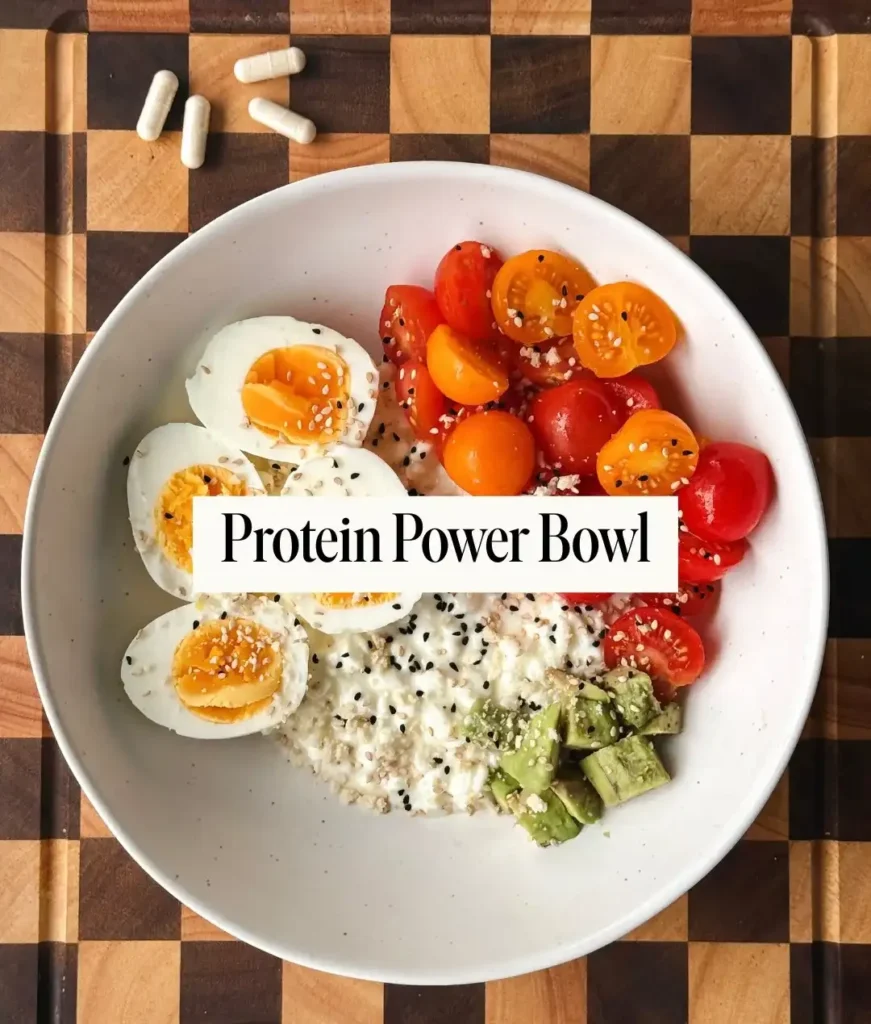 White bowl with halved boiled eggs, cottage cheese, cherry tomatoes and diced avocado sprinkled with sesame seeds