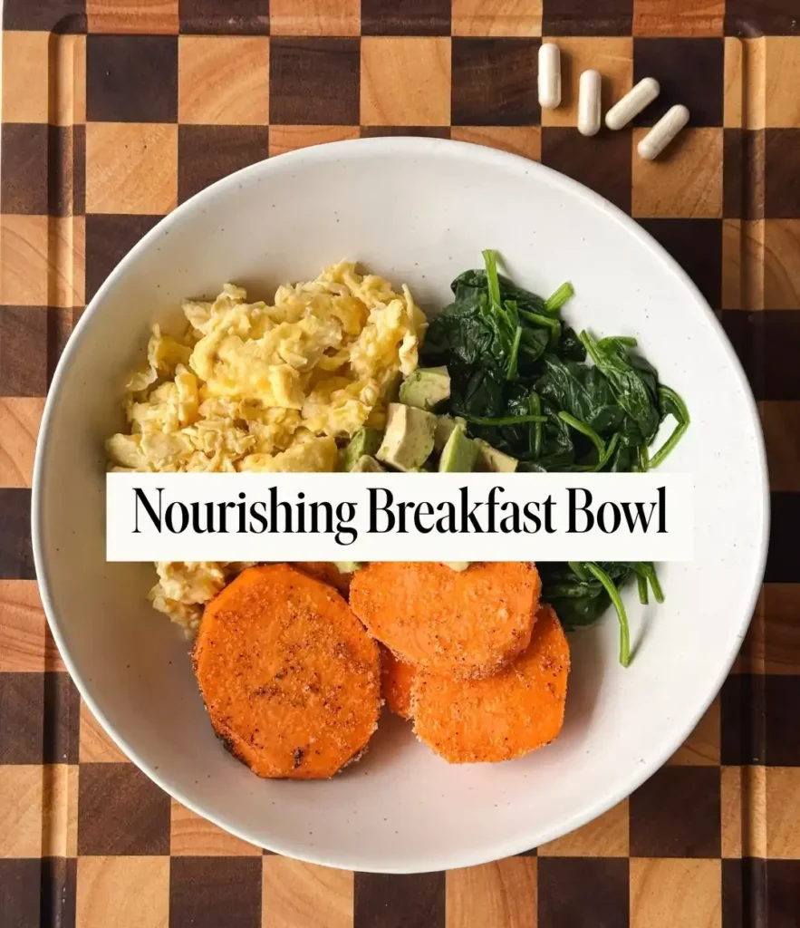 White bowl with scrambled eggs, cooked spinach, diced avocado and roasted seasoned sweet potato rounds