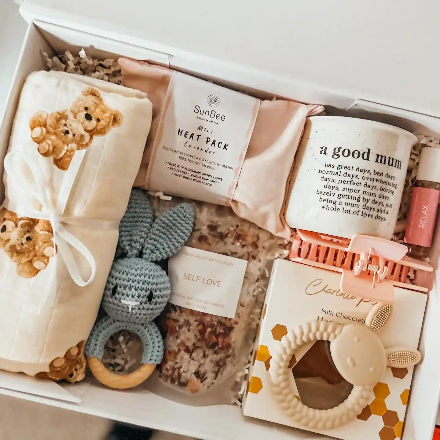 Gift box with a mug printed with a good mum message, a pink claw clip, a honeycomb milk chocolate treat, a bear print muslin wrap, a crochet bunny rattle and a lamb teether