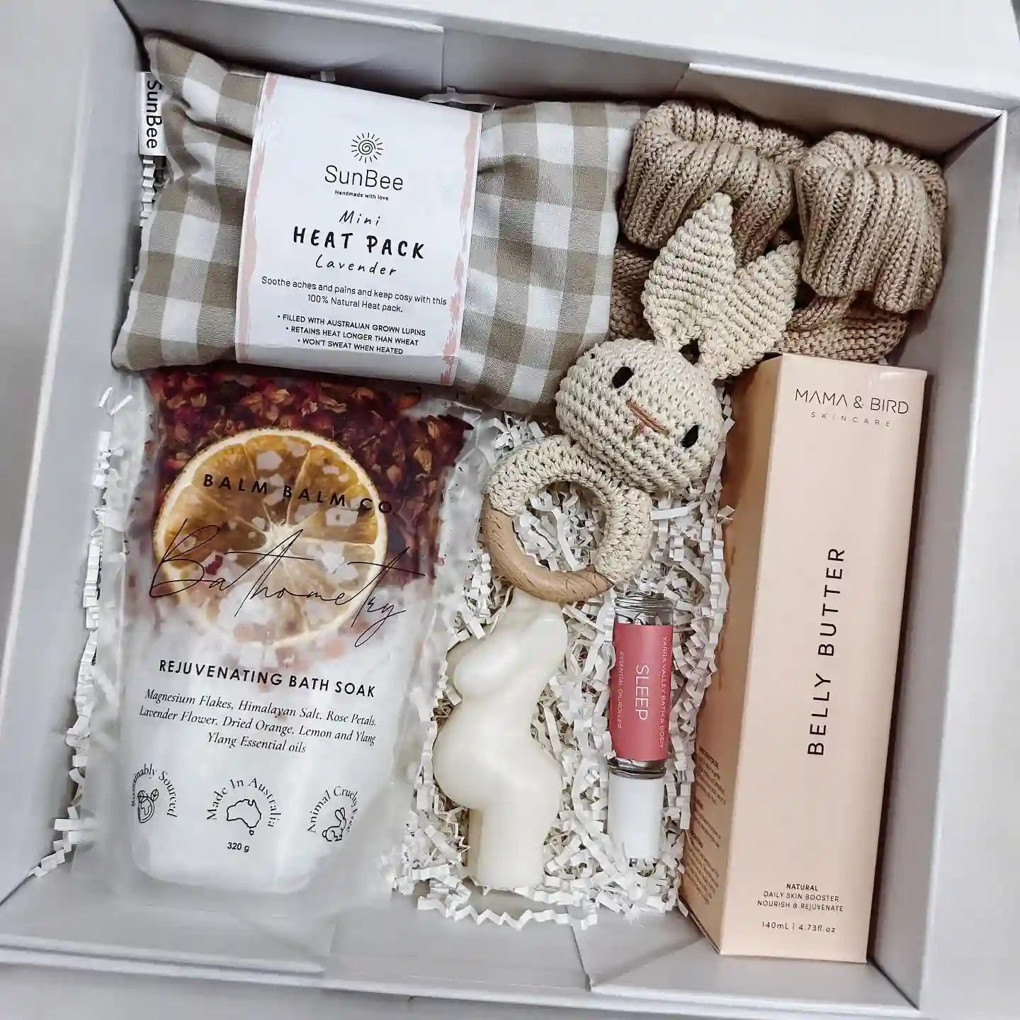 Gift box with belly butter, a belly shaped candle, a gingham lavender heat pack, a bath soak, a sleep roll-on, a cream crochet bunny rattle and soft knit baby pieces