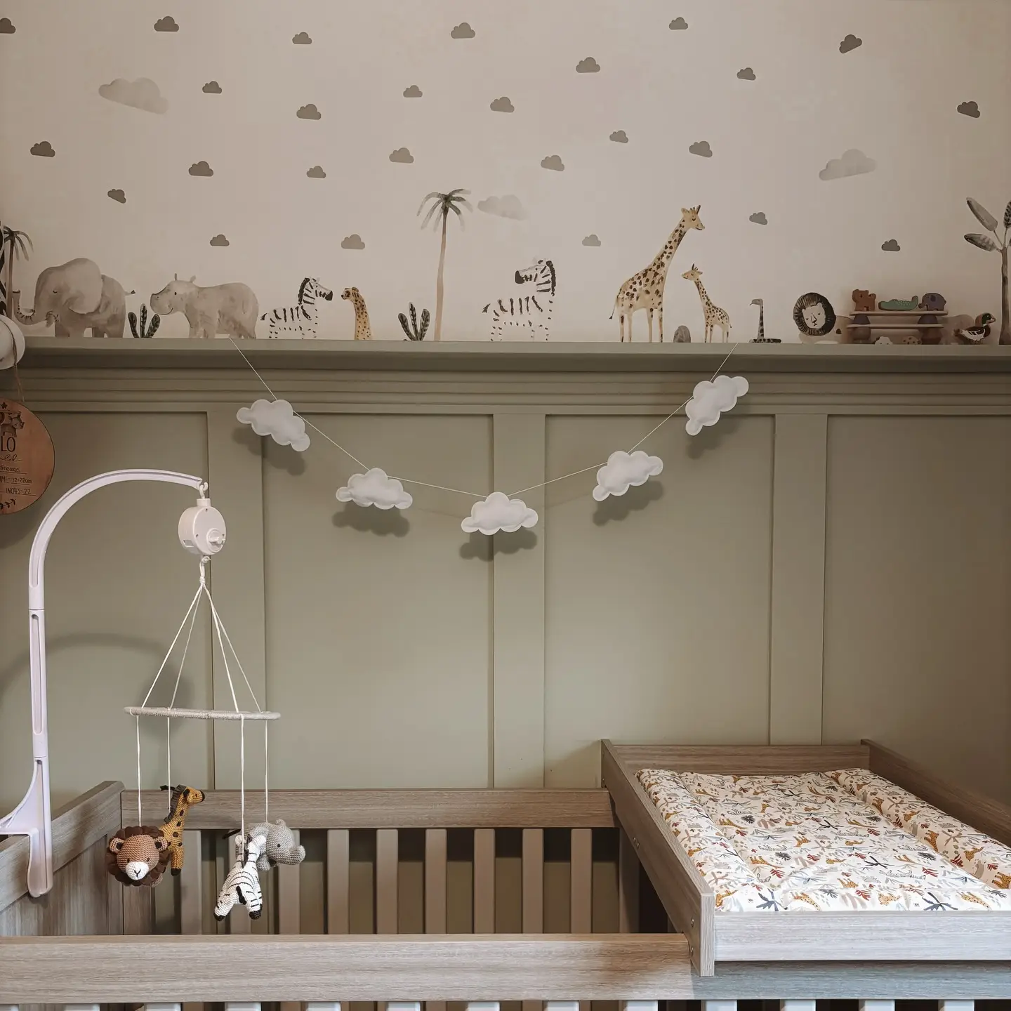 Nursery with sage green panelling, safari wall decals, a cloud garland and a wooden cot