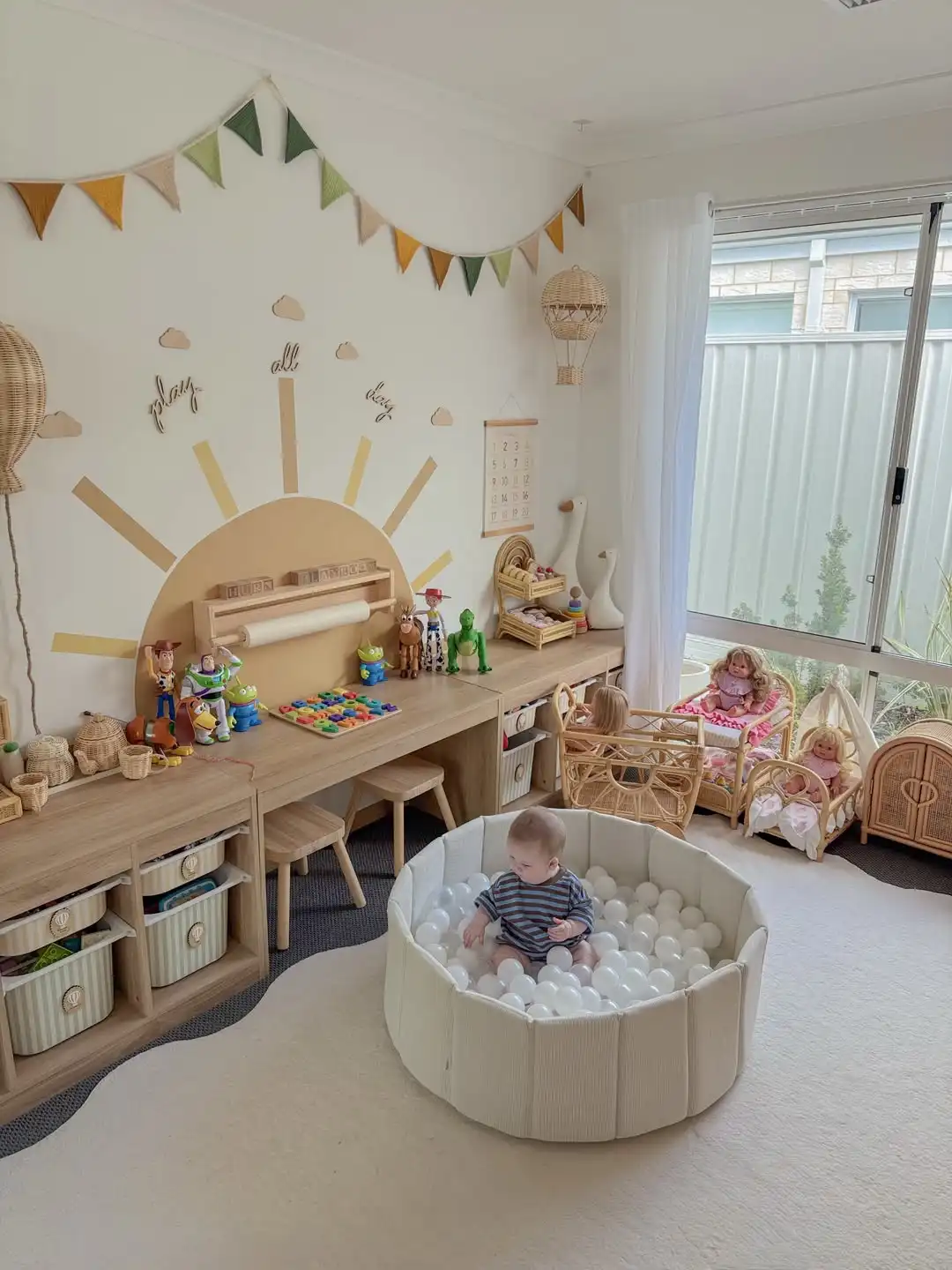 Long wood craft counter with striped bins in frames underneath, a paper roll holder, two small stools and a painted sun on the wall