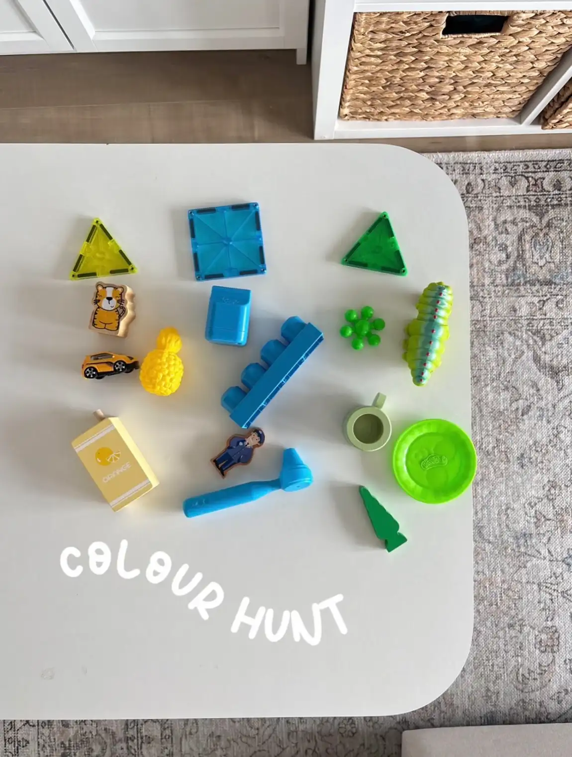 Colour hunt game with blue and green toys, blocks and magnetic tiles laid out on a white table
