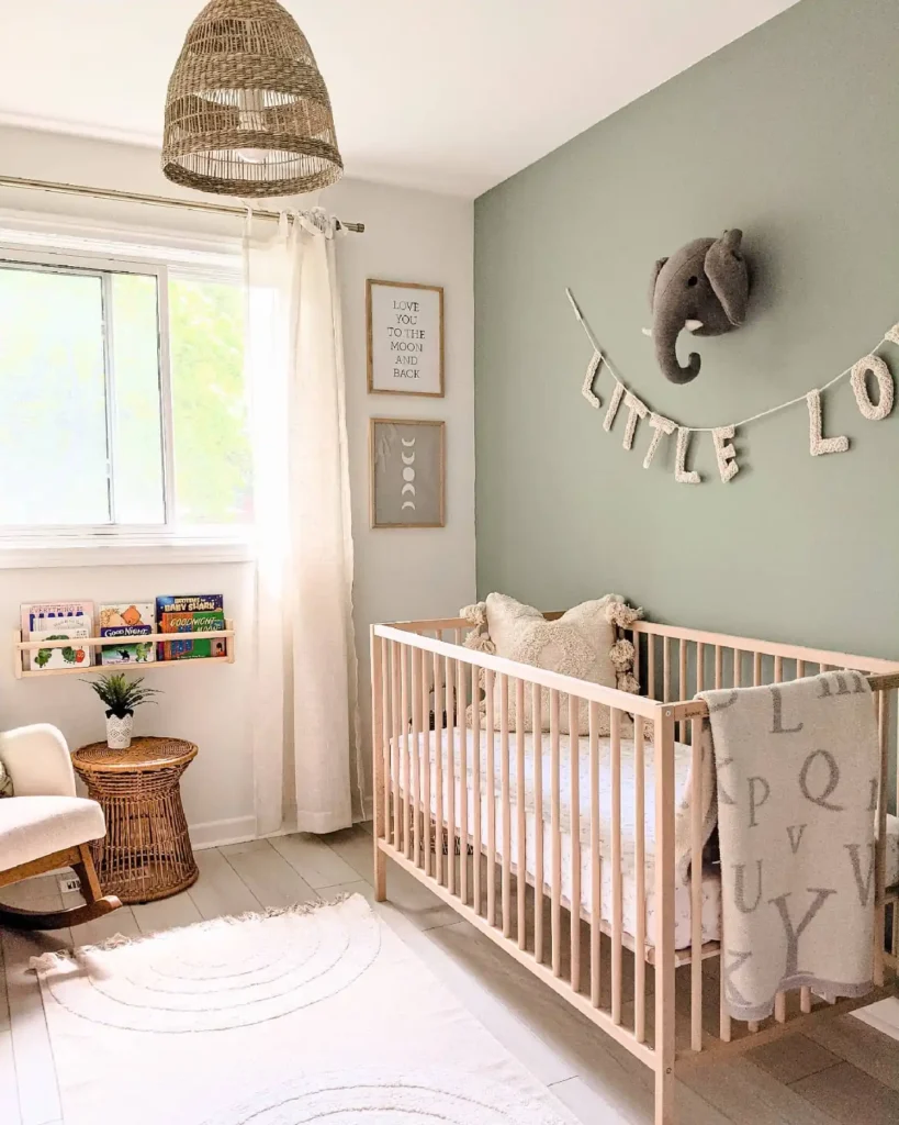 Nursery with a sage green accent wall, gray felt elephant head, knitted letter garland and natural wood crib