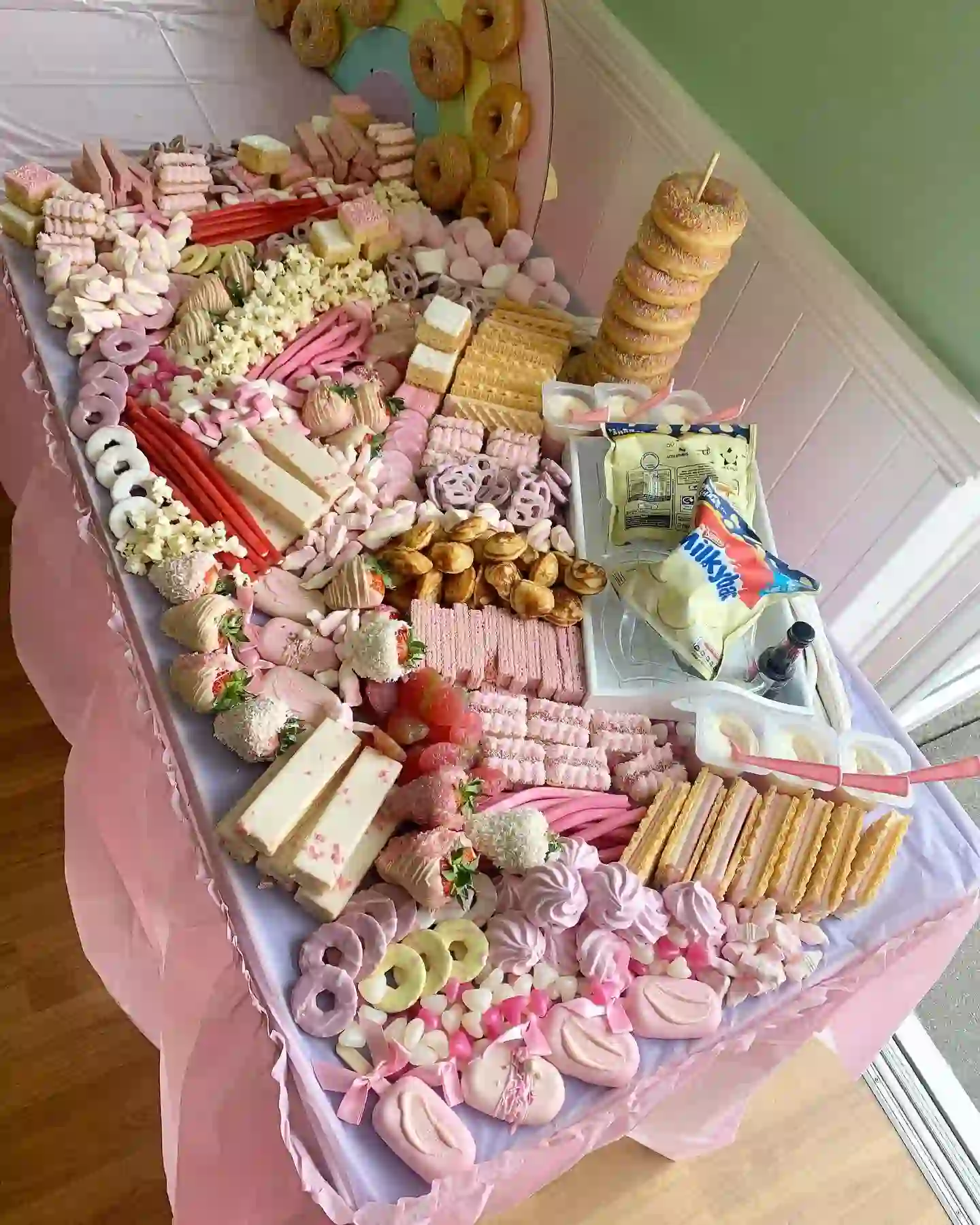 Pink and white birthday sweet table with dipped strawberries, marshmallows, wafers, meringues and a tower of doughnuts