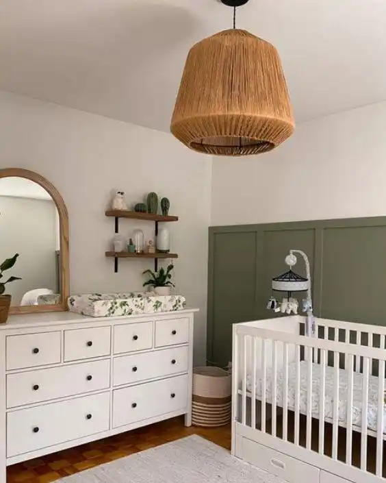 Nursery with a large jute pendant light, olive green paneling, a white crib and a white dresser with an arched mirror