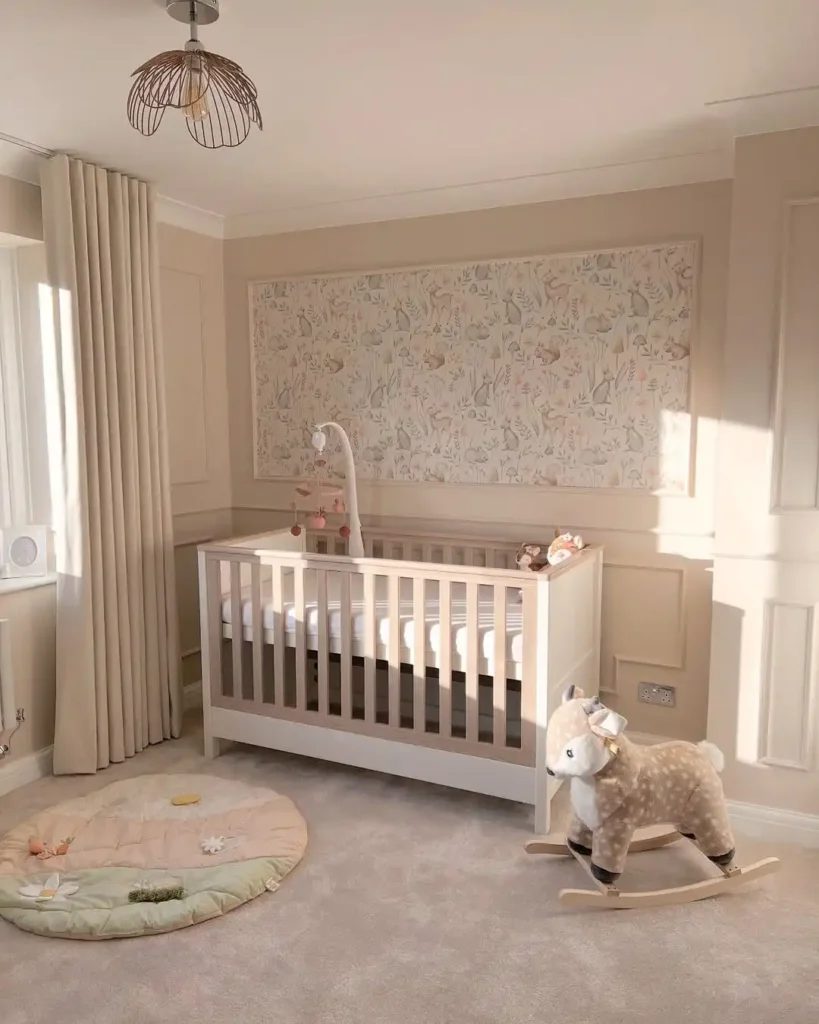 Beige nursery with a framed woodland animal wallpaper panel above a white and wood crib, with a deer rocker and round play mat