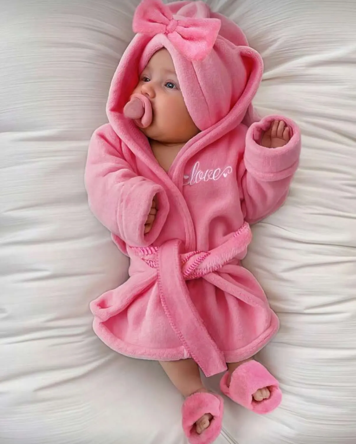Baby in a pink fleece hooded robe with a bow and fuzzy slippers