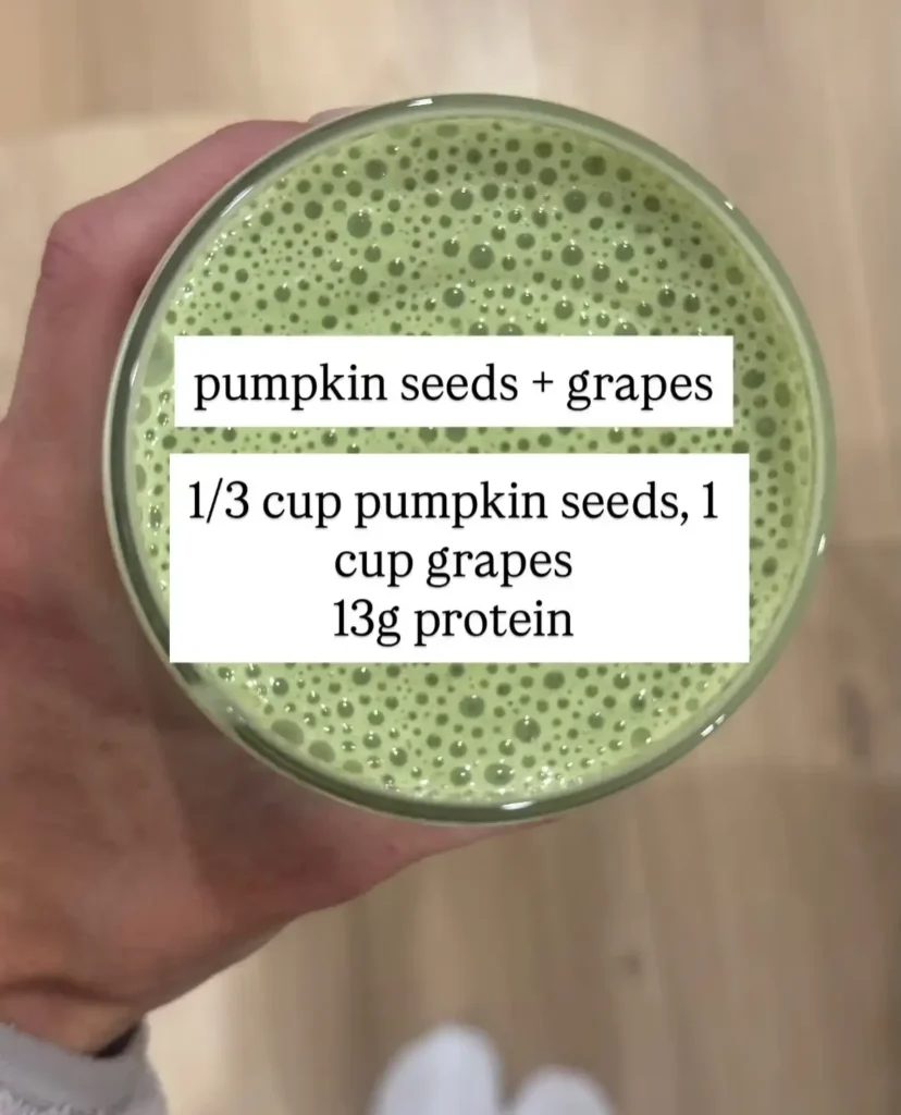 Top view of a pale green frothy smoothie in a glass with a label listing one third cup pumpkin seeds, one cup grapes and 13g protein