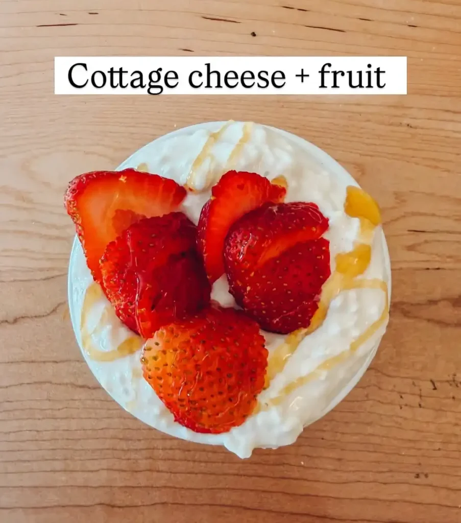 Small bowl of cottage cheese topped with sliced strawberries and a drizzle of honey on a wooden table