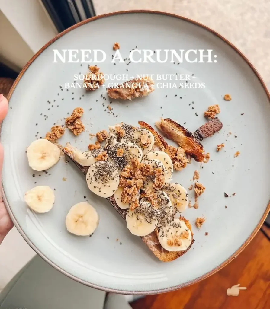 Blue plate with sourdough toast spread with nut butter and topped with banana slices, granola and chia seeds