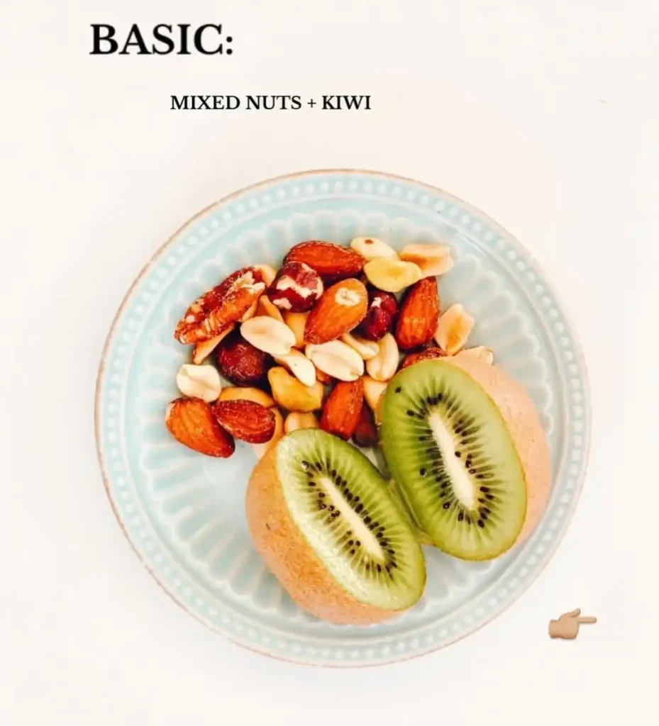 Pale blue plate with a pile of mixed nuts including almonds and peanuts next to two halves of a kiwi