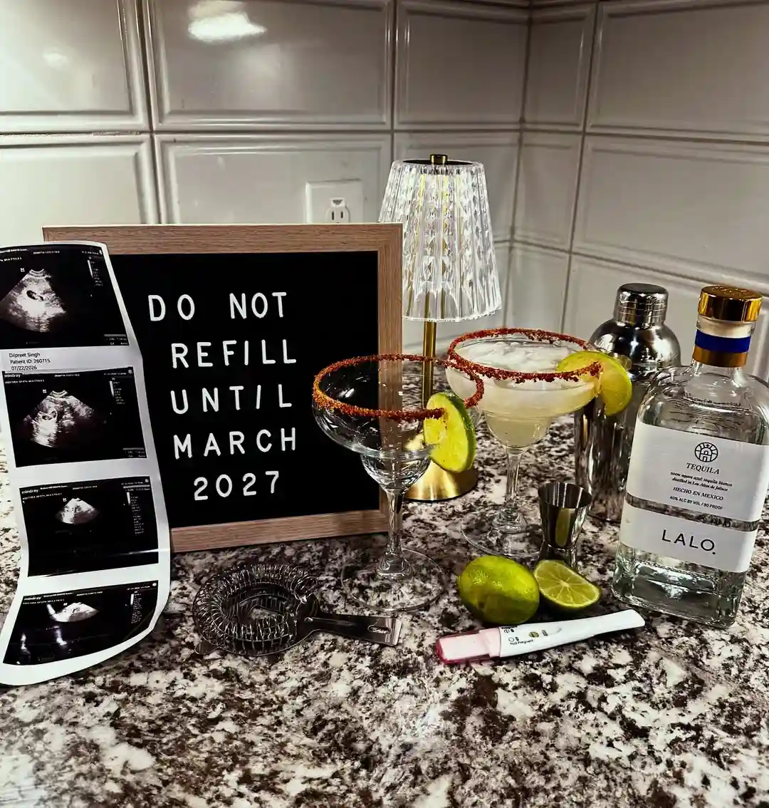 Kitchen counter bar with a letter board reading "Do not refill until March 2027", two rimmed cocktail glasses, a shaker, limes, a tequila bottle, a pregnancy test and an ultrasound strip