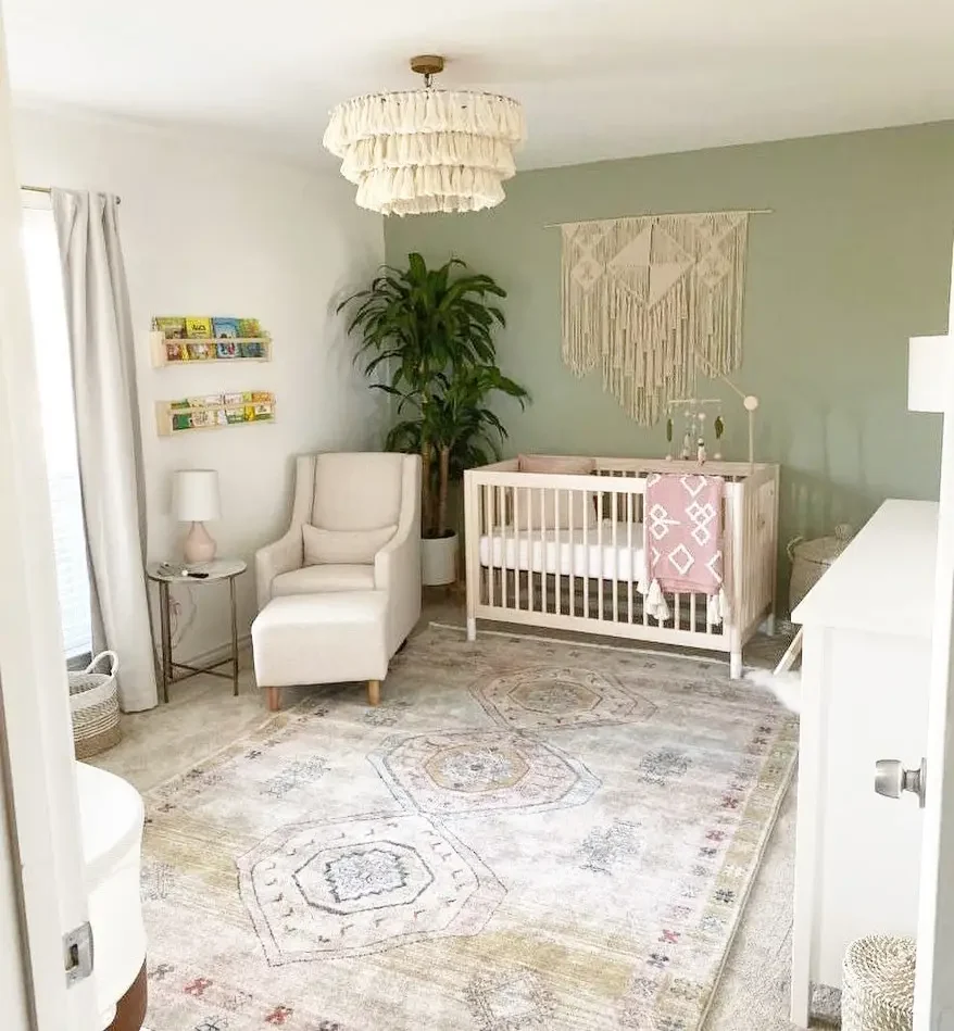 Nursery with a sage green feature wall, macrame hanging, white crib and a cream armchair