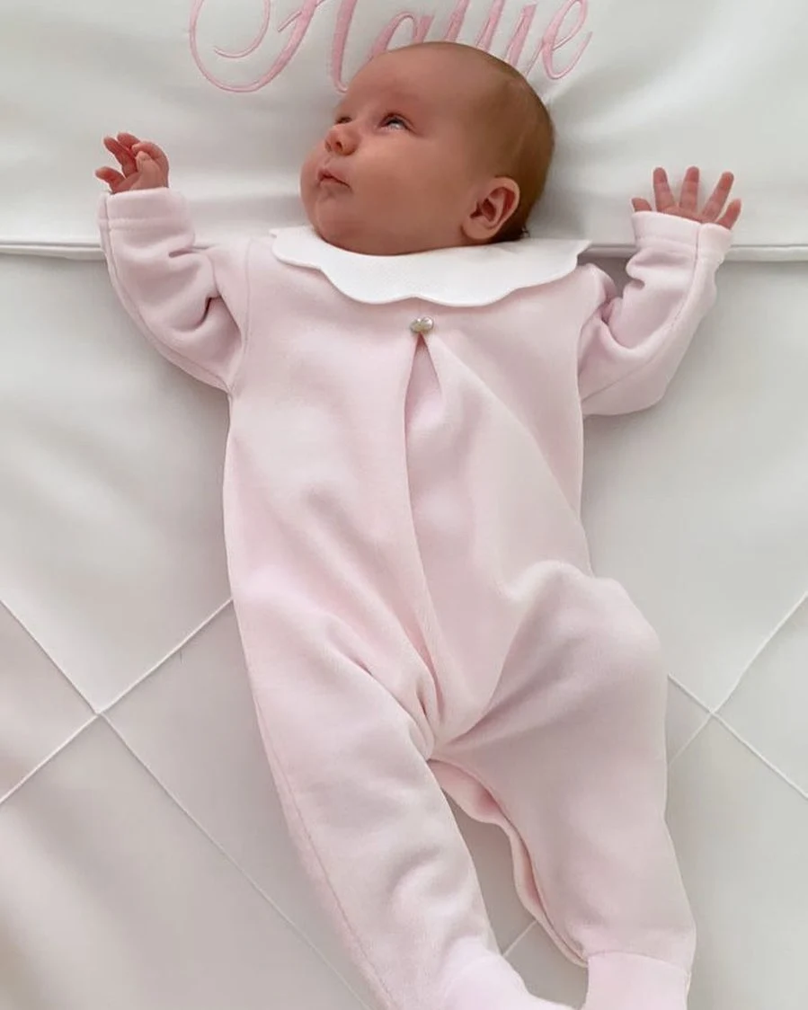Newborn in a pale pink velour footed sleeper with a scalloped white collar