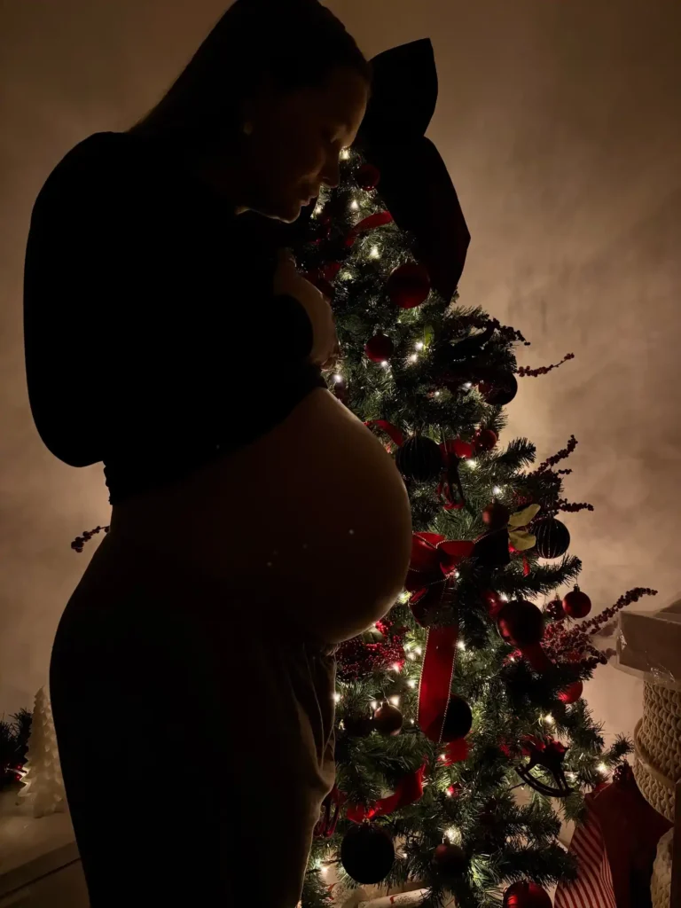 Silhouette of a pregnant woman holding her bump in front of a lit Christmas tree