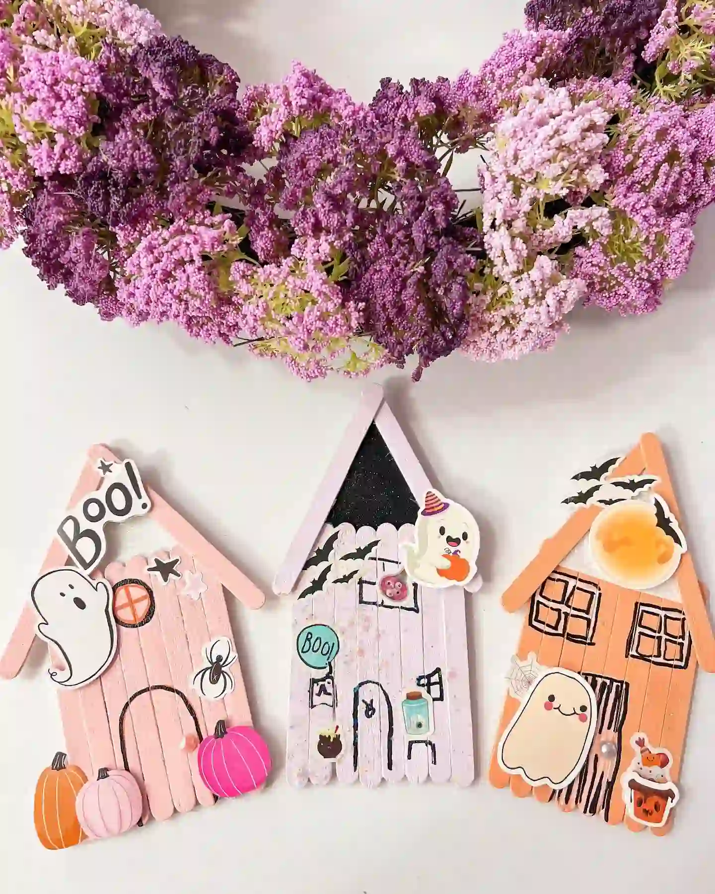 Dollar tree crafts for kids: three pastel craft stick haunted houses in blush pink, soft lilac and peach with pointed roofs, marker doors and windows, and ghost, bat and pumpkin stickers