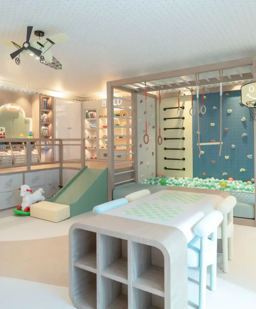Playroom with lit cubbies showing toy cars, planes and dinosaurs, drawers with etched icons below, wooden crates on a raised platform and a craft table with cubby ends
