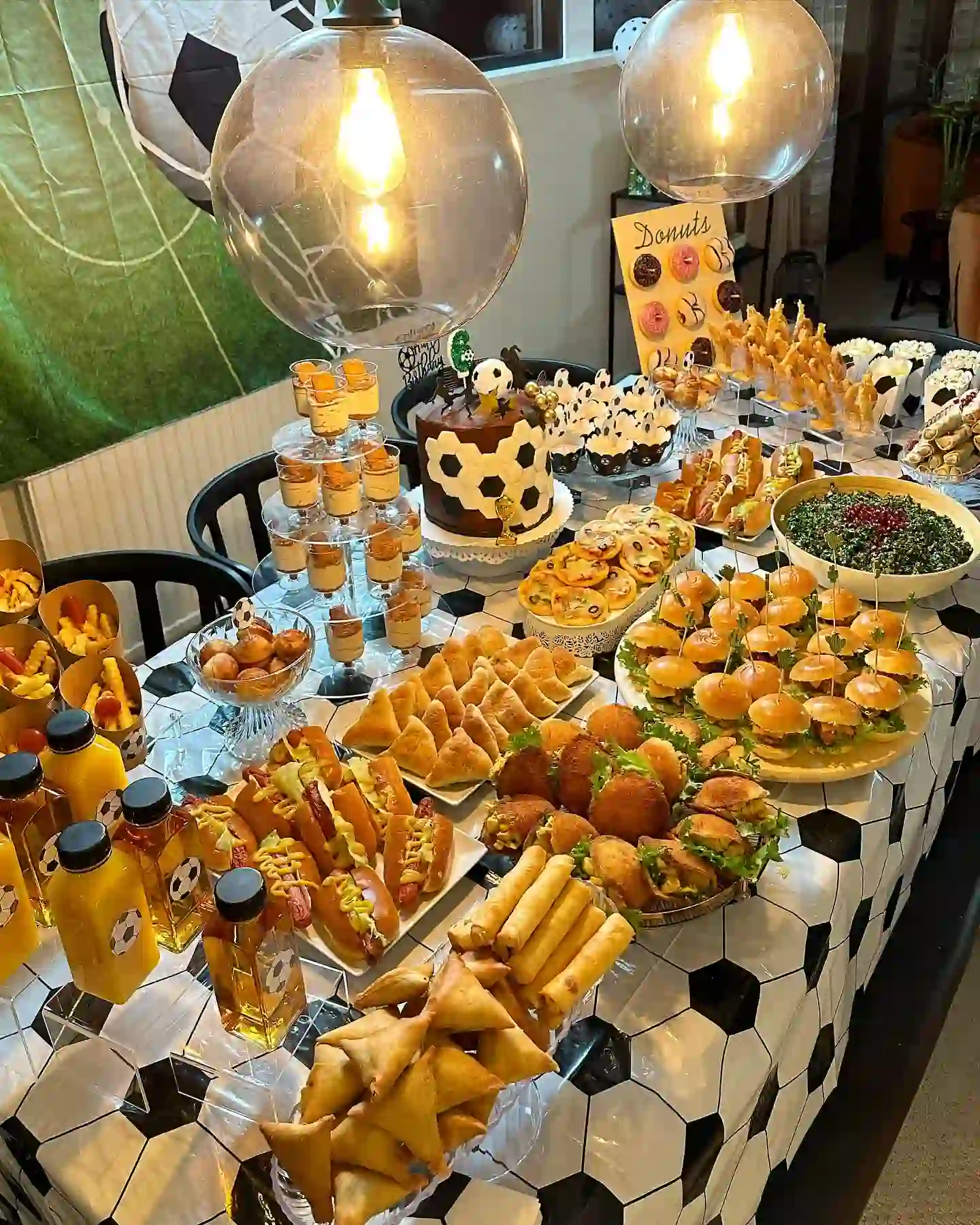 Football birthday table with mini burgers on sticks, hot dogs, samosas, spring rolls and a ball-print tablecloth
