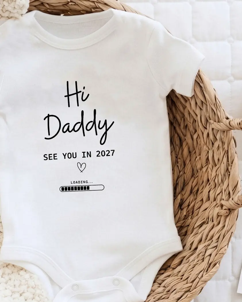 Small white onesie in a woven basket printed with hi daddy, see you in 2027, a tiny heart and a nearly full loading bar