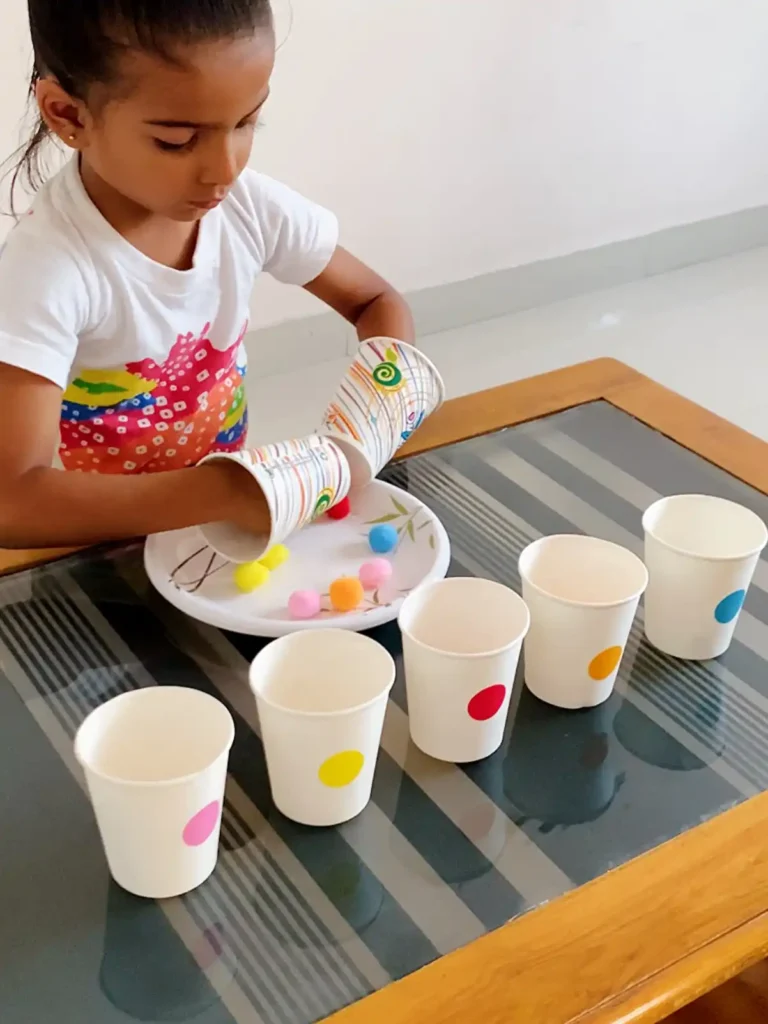 Girl wearing paper cups on both hands to pick up pom poms and sort them into color matched cups